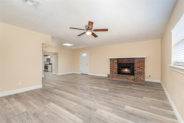 unfurnished living room with a textured ceiling, light wood-type flooring, a brick fireplace, and ceiling fan