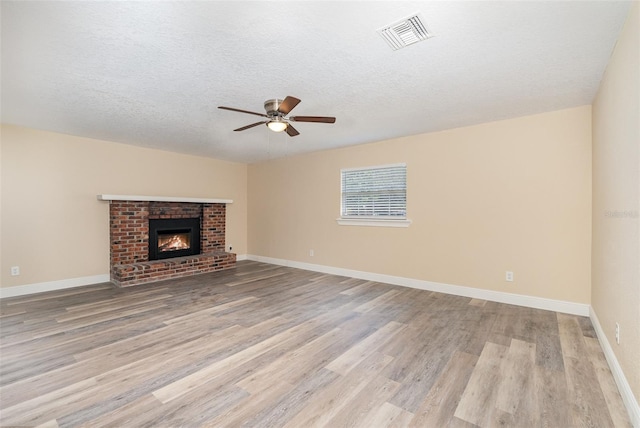 unfurnished living room featuring ceiling fan, a fireplace, a textured ceiling, and light wood-type flooring