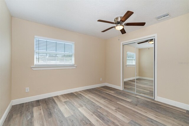 unfurnished bedroom with a textured ceiling, light wood-type flooring, a closet, and ceiling fan