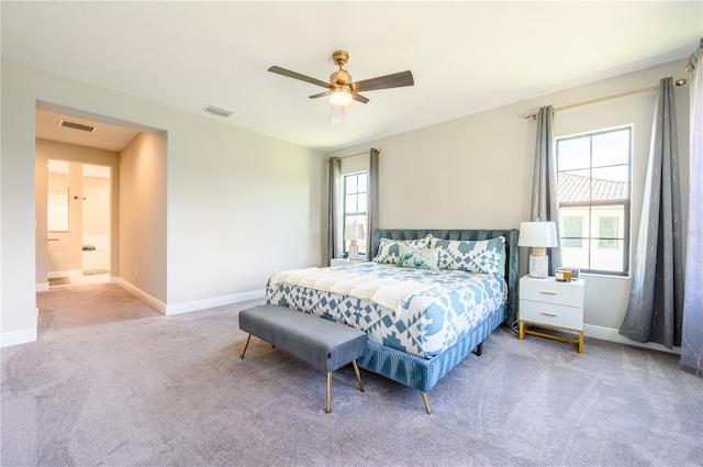 bedroom featuring multiple windows, light colored carpet, ensuite bath, and ceiling fan