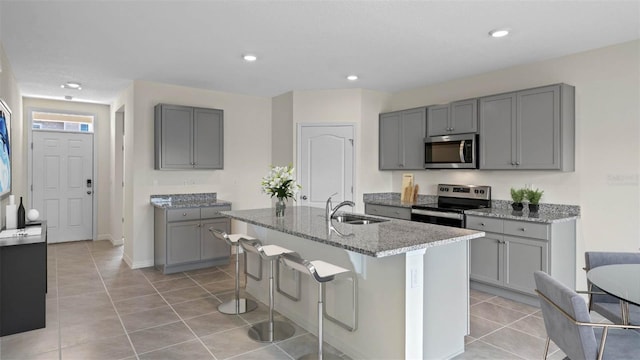 kitchen featuring a kitchen island with sink, stainless steel appliances, and gray cabinetry