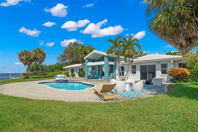 rear view of property with a water view, a lawn, stucco siding, an outdoor pool, and a patio area