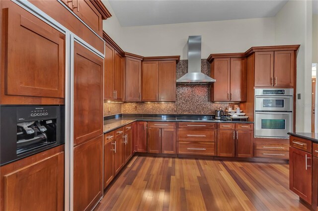 kitchen with decorative backsplash, black electric stovetop, wall chimney exhaust hood, wood-type flooring, and double oven