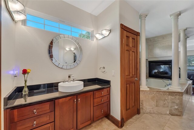 bathroom with a relaxing tiled tub, ornate columns, vanity, and tile patterned floors