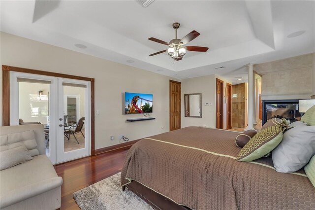 bedroom with ceiling fan, a raised ceiling, french doors, and wood-type flooring