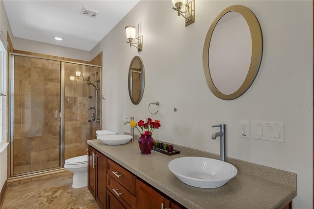 bathroom featuring a shower with shower door, toilet, dual vanity, and tile patterned flooring