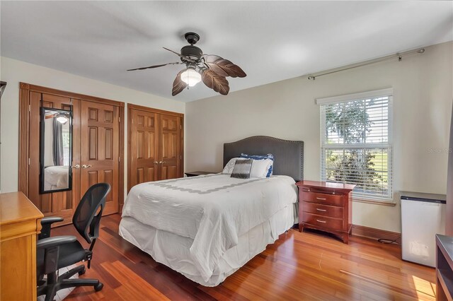 bedroom with ceiling fan, multiple closets, and wood-type flooring