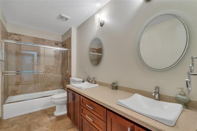 full bathroom with bath / shower combo with glass door, toilet, dual bowl vanity, and tile patterned floors