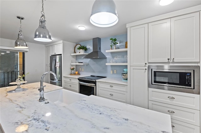 kitchen featuring wall chimney range hood, white cabinets, sink, decorative light fixtures, and stainless steel appliances