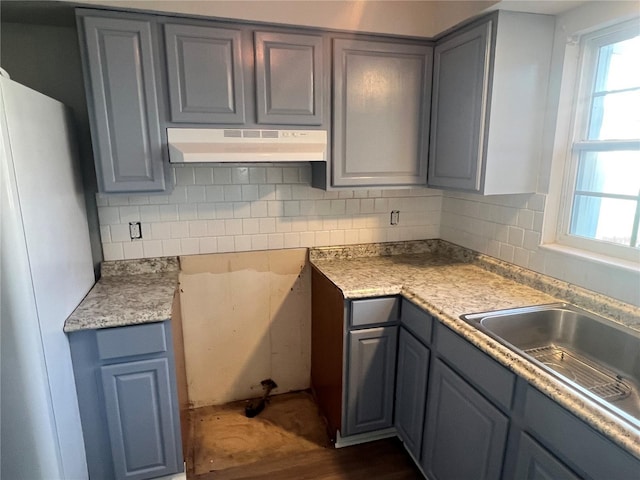 kitchen with a sink, tasteful backsplash, gray cabinets, and under cabinet range hood