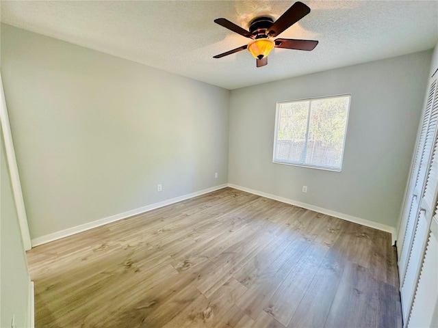 unfurnished bedroom featuring a closet, ceiling fan, a textured ceiling, wood finished floors, and baseboards