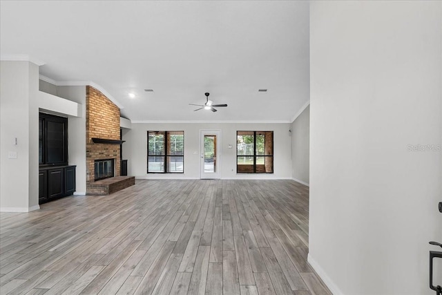 unfurnished living room with brick wall, light hardwood / wood-style floors, crown molding, and a brick fireplace