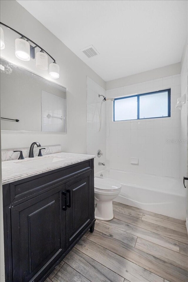 full bathroom with tiled shower / bath combo, vanity, toilet, and hardwood / wood-style flooring