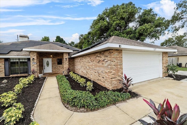 ranch-style house with a garage, driveway, solar panels, and brick siding