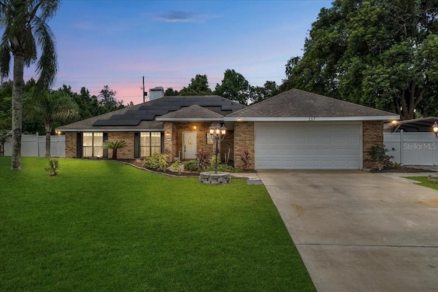 view of front of property featuring a garage, driveway, solar panels, a lawn, and fence