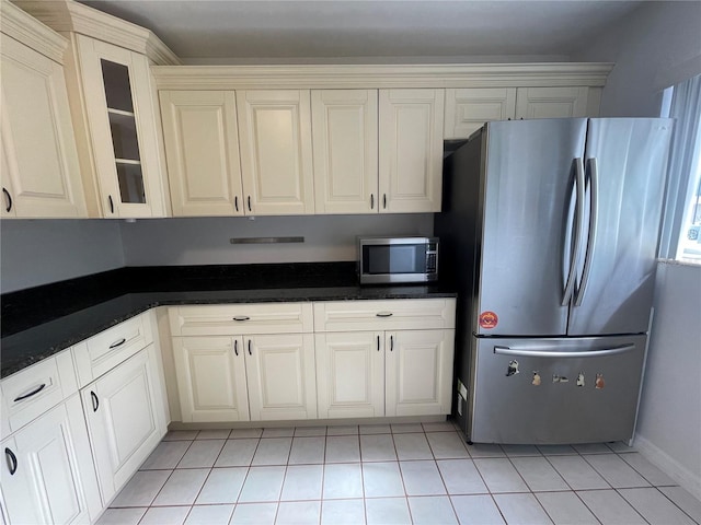 kitchen featuring appliances with stainless steel finishes, light tile patterned flooring, dark stone countertops, and white cabinetry