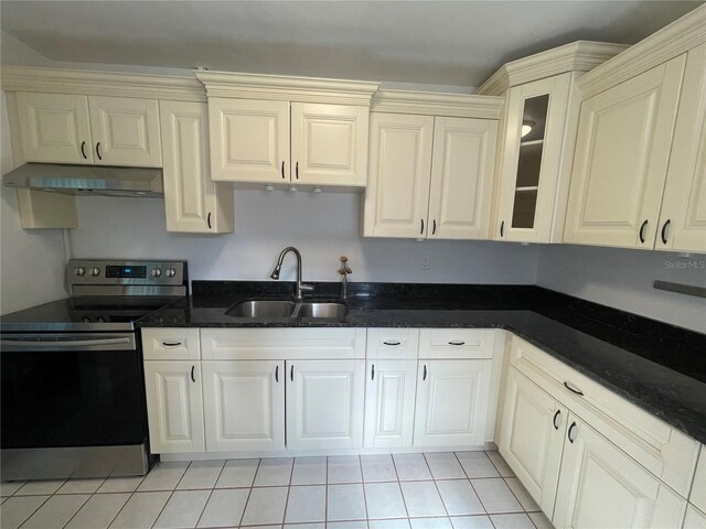 kitchen featuring stainless steel range with electric cooktop, light tile patterned floors, dark stone countertops, and sink