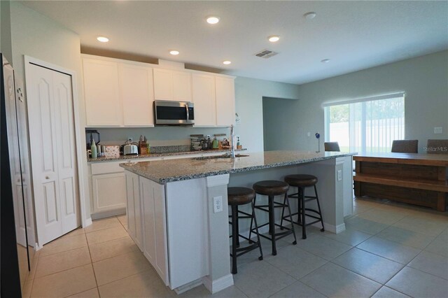 kitchen featuring a kitchen island with sink, white cabinetry, dark stone countertops, and light tile patterned flooring