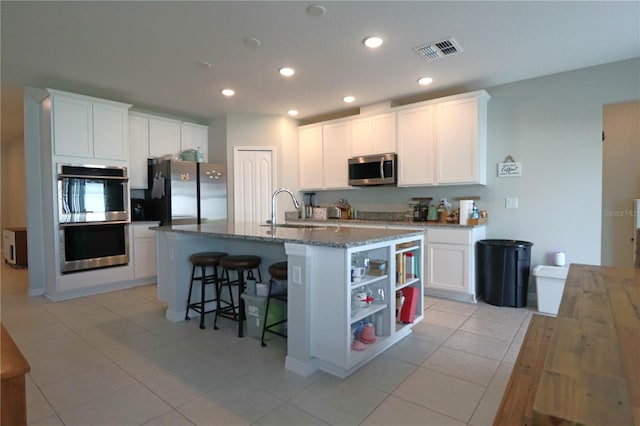 kitchen with white cabinets, appliances with stainless steel finishes, sink, an island with sink, and dark stone counters