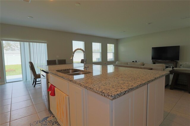 kitchen with an island with sink, a wealth of natural light, light stone counters, and sink