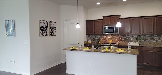 kitchen featuring an island with sink, tasteful backsplash, decorative light fixtures, dark stone counters, and dark hardwood / wood-style floors