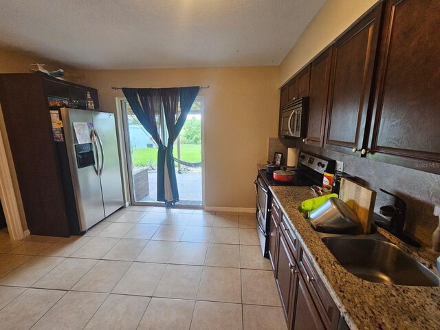 kitchen featuring dark brown cabinets, light stone counters, sink, stainless steel appliances, and light tile patterned floors