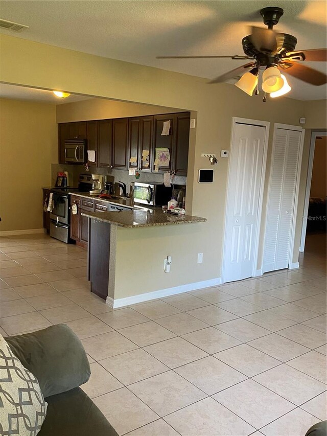 kitchen featuring dark stone counters, dark brown cabinets, stainless steel appliances, light tile patterned floors, and ceiling fan