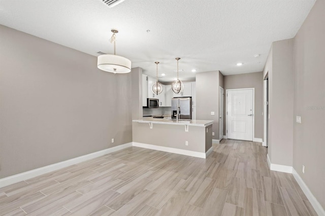 kitchen with a kitchen breakfast bar, appliances with stainless steel finishes, white cabinetry, kitchen peninsula, and pendant lighting