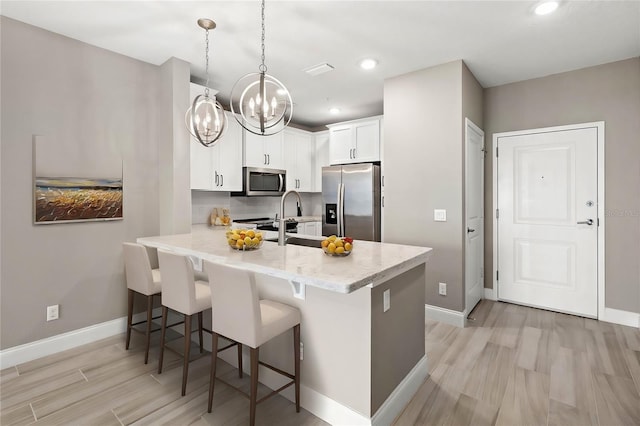 kitchen featuring decorative light fixtures, a breakfast bar area, appliances with stainless steel finishes, white cabinets, and a peninsula