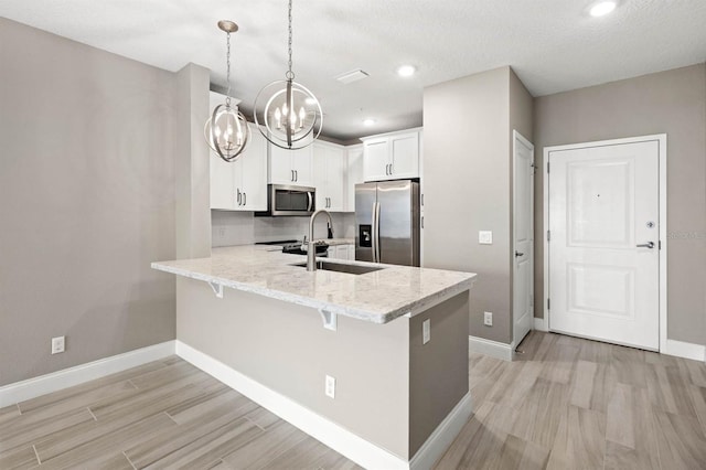 kitchen with pendant lighting, light wood finished floors, stainless steel appliances, white cabinets, and a peninsula