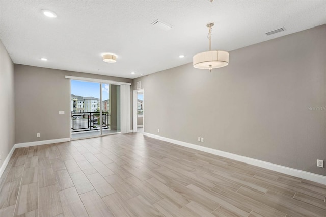 empty room with baseboards, visible vents, a textured ceiling, and light wood finished floors