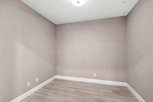 unfurnished room with baseboards, a textured ceiling, and wood finish floors