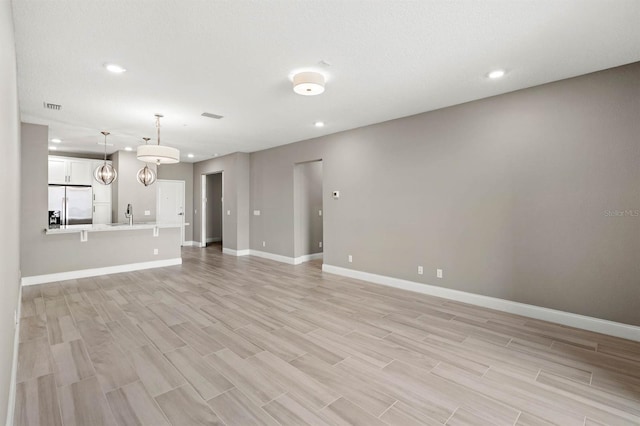 unfurnished living room with recessed lighting, a sink, visible vents, light wood-style floors, and baseboards