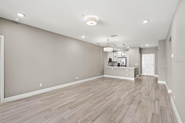 unfurnished living room featuring a textured ceiling, recessed lighting, light wood-style flooring, and baseboards