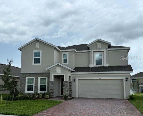 view of front of home featuring a garage, stone siding, decorative driveway, stucco siding, and a front yard