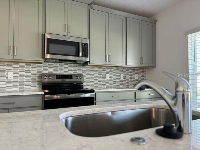 kitchen featuring sink, appliances with stainless steel finishes, light stone counters, tasteful backsplash, and gray cabinetry