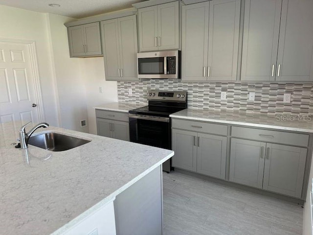 kitchen with appliances with stainless steel finishes, backsplash, sink, light stone countertops, and gray cabinets