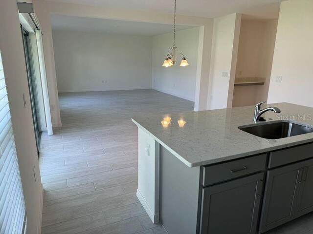 kitchen with gray cabinetry, light hardwood / wood-style floors, light stone countertops, sink, and an inviting chandelier