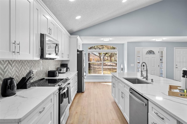 kitchen with sink, stainless steel appliances, light hardwood / wood-style floors, vaulted ceiling, and white cabinets