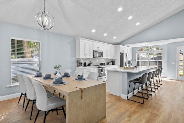 kitchen featuring white cabinets, light wood-type flooring, stainless steel appliances, and a kitchen island with sink