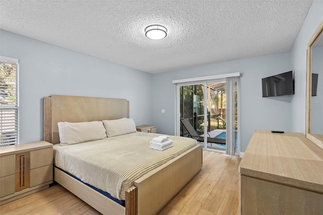 bedroom featuring access to exterior, a textured ceiling, light hardwood / wood-style floors, and multiple windows