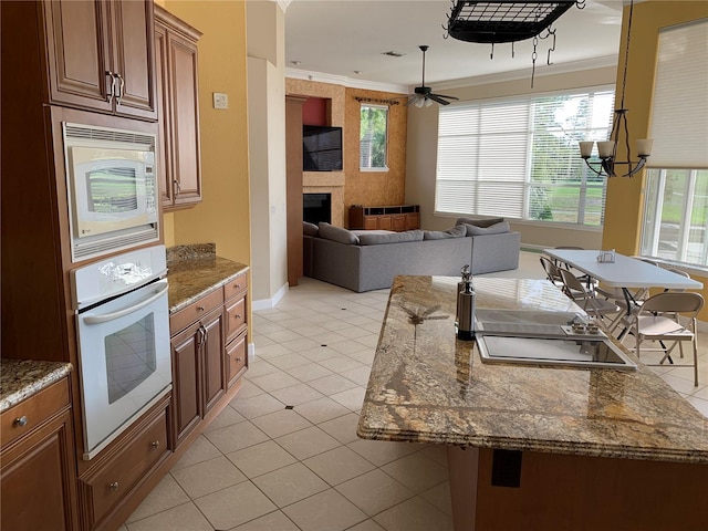 kitchen with ceiling fan, a large fireplace, a breakfast bar, light tile patterned floors, and white appliances