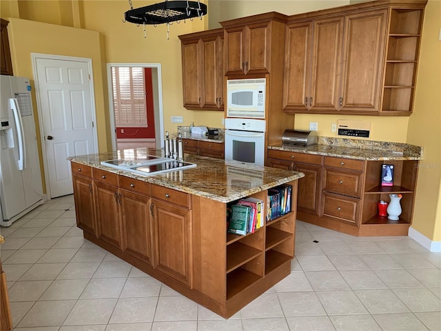 kitchen with a high ceiling, stone counters, white appliances, a kitchen island with sink, and light tile patterned floors