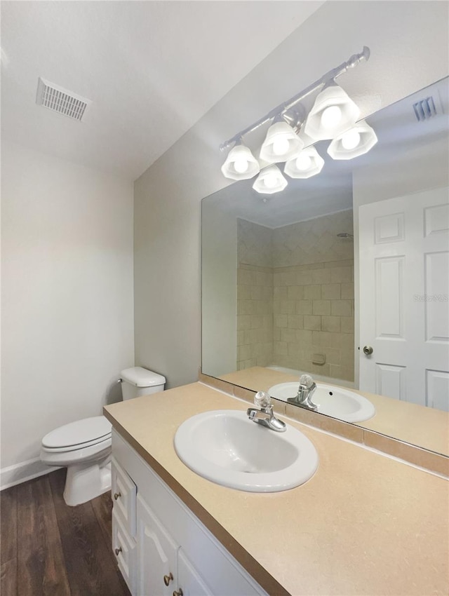 bathroom featuring hardwood / wood-style floors, tiled shower, vanity, and toilet