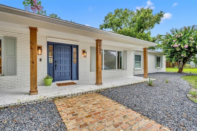 doorway to property featuring covered porch and brick siding