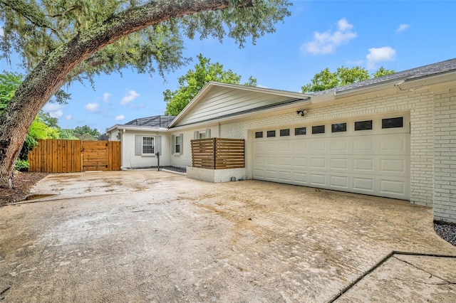 ranch-style house featuring concrete driveway, an attached garage, a gate, fence, and brick siding