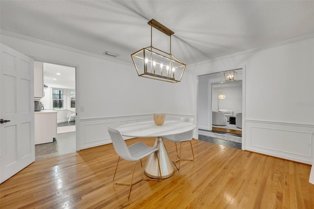 dining space with light wood-type flooring, a wainscoted wall, visible vents, and crown molding