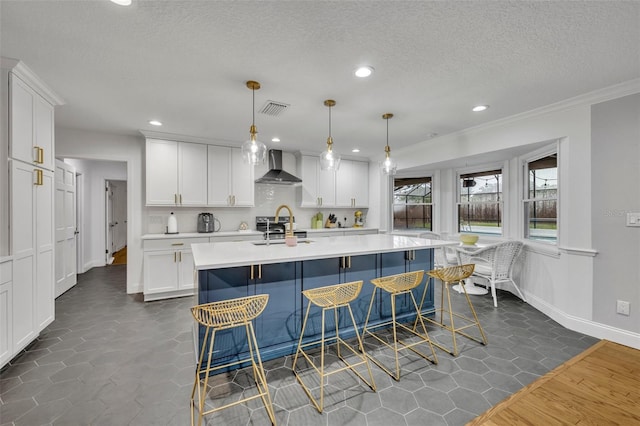 kitchen featuring a breakfast bar area, visible vents, white cabinets, light countertops, and wall chimney range hood