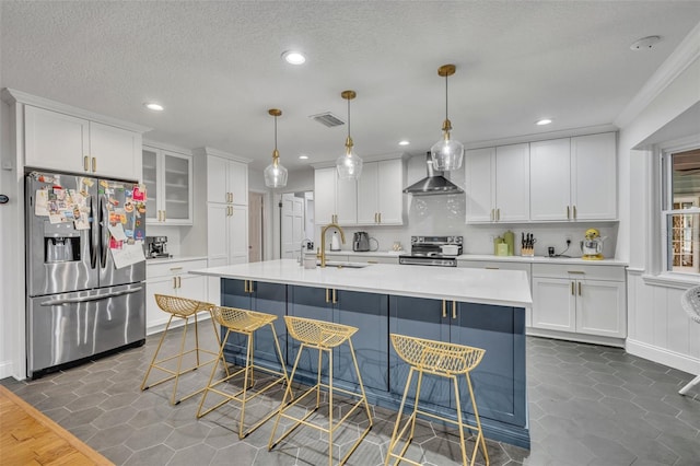 kitchen with visible vents, stainless steel appliances, light countertops, wall chimney range hood, and white cabinetry