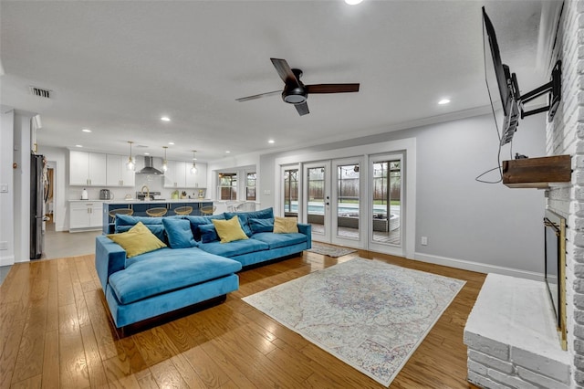 living area with light wood-type flooring, a large fireplace, a healthy amount of sunlight, and french doors